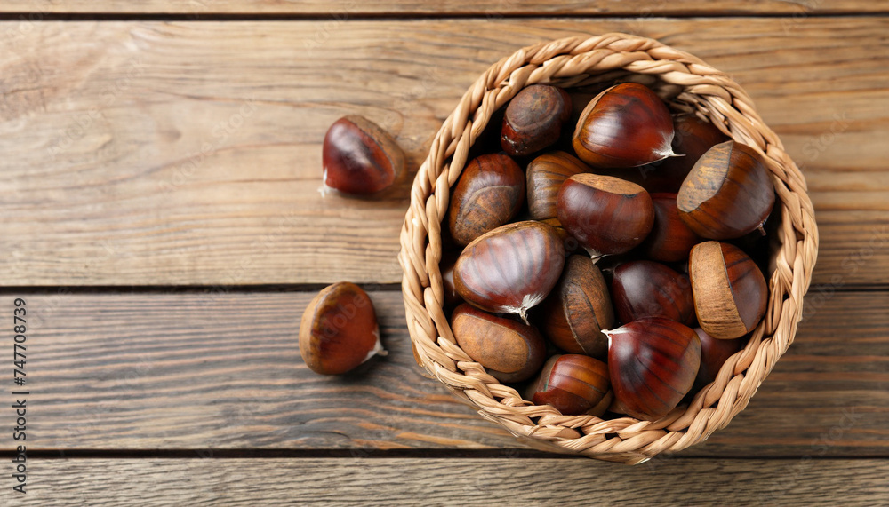 Sweet fresh edible chestnuts in wicker bowl on wooden table, top view. Space for text Sweet fresh edible chestnuts in wicker bowl on wooden table, top view. Space for text