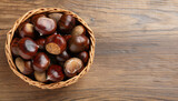 Sweet fresh edible chestnuts in wicker bowl on wooden table, top view. Space for text