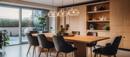 A wooden table is surrounded by chairs in a contemporary dining room. A pendant light hangs above the table, casting a warm glow over the room.