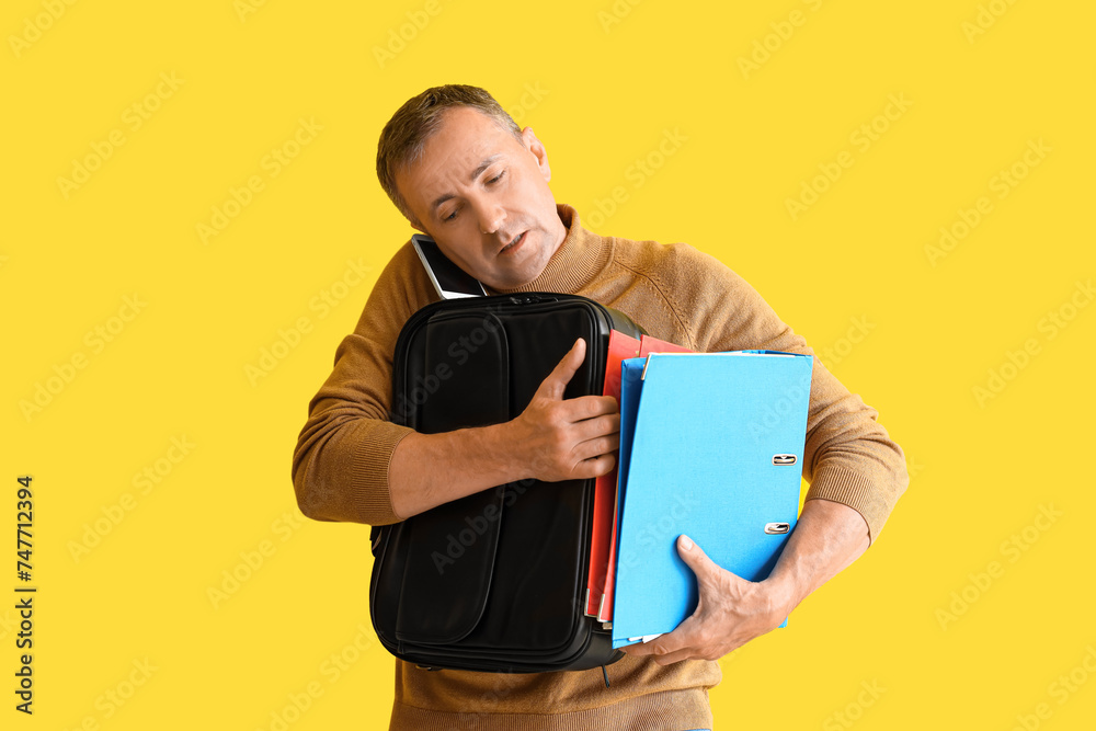 Stressed mature man with briefcase talking by mobile phone on yellow background. Deadline concept