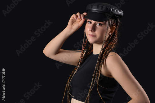 Young woman with dreadlocks in stylish hat on dark background, closeup