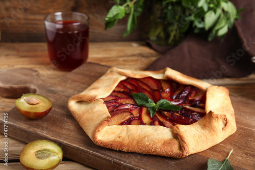 Board of delicious plum galette with mint on wooden background