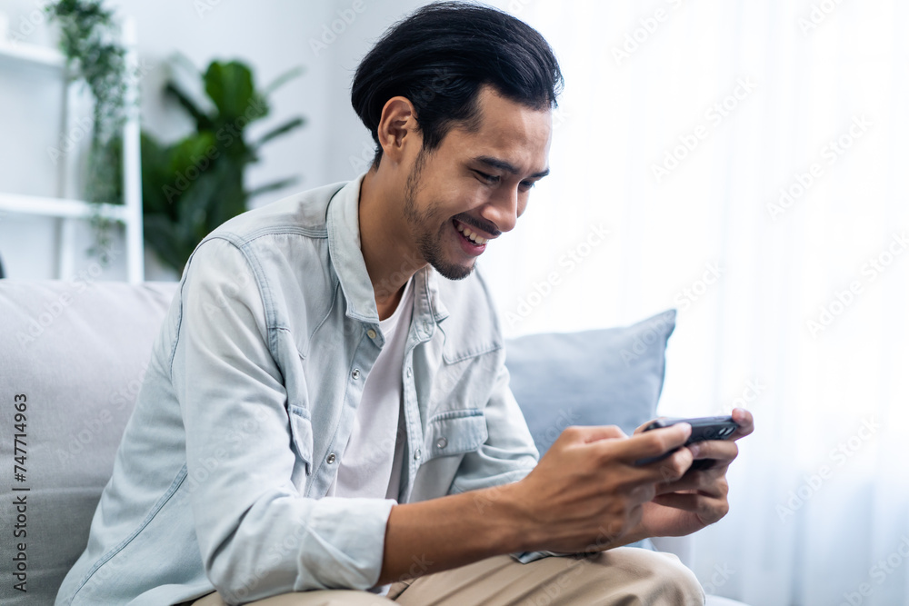 Asian young handsome man gamer play mobile game on smartphone at home. 