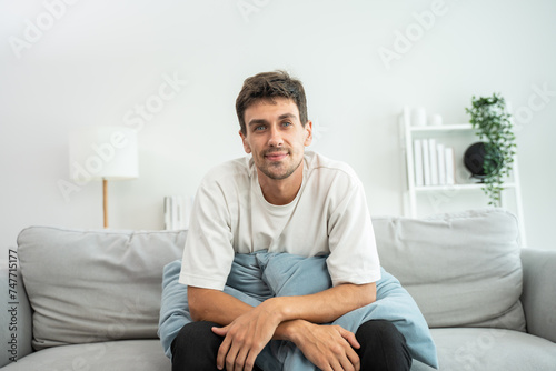 Portrait of young Caucasian man sitting on sofa in living room at home.  © Kawee