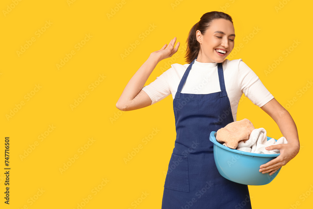 Portrait of happy young housewife in apron with dirty laundry on yellow background Portrait of happy young housewife in apron with dirty laundry on yellow background
