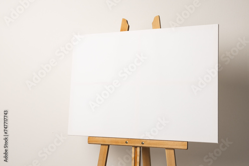 A blank canvas is positioned on a wooden easel against a neutral background, with copy space