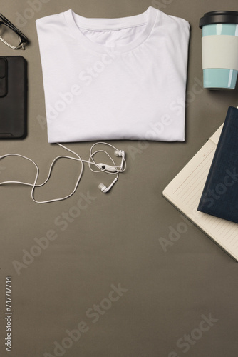 A neatly folded white t-shirt is surrounded by everyday items including a smartphone, earphones, a n