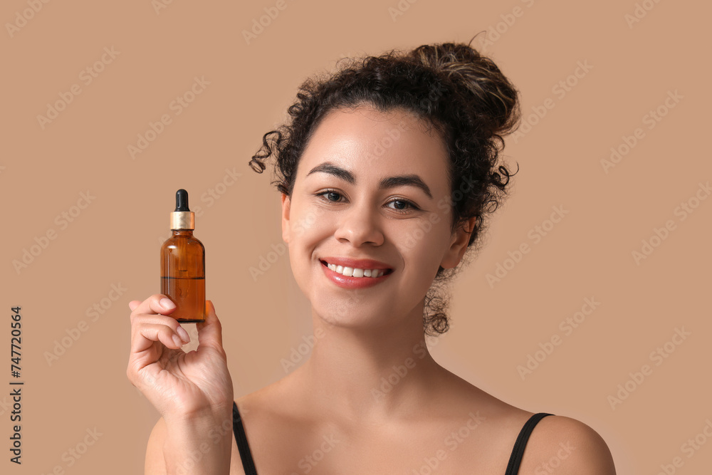 Fototapeta premium Beautiful young African-American woman with bottle of cosmetic oil on brown background
