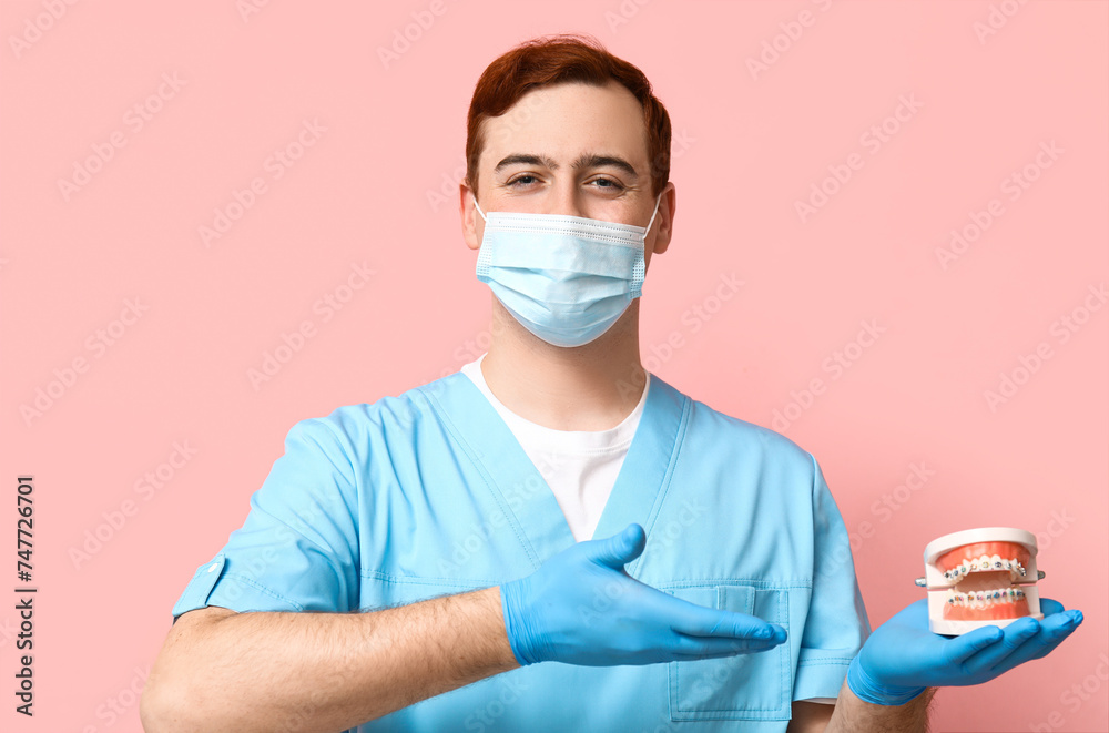 Male dentist in mask showing jaw model on pink background. World Dentist Day Male dentist in mask showing jaw model on pink background. World Dentist Day
