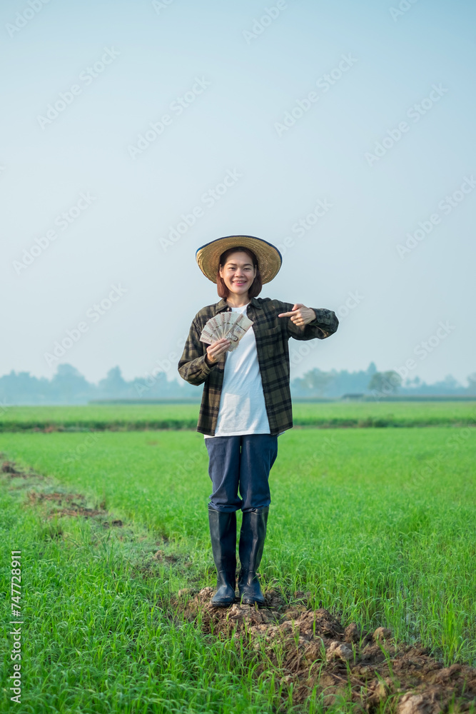 Asian female farmer dressed in brown blouses, jeans Stand and pose holding banknote money with a smiling expression. Asian female farmer dressed in brown blouses, jeans Stand and pose holding banknote money with a smiling expression.