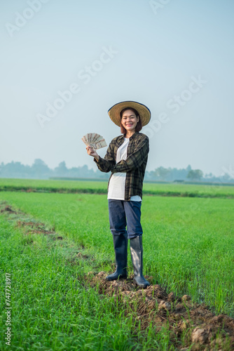 Asian female farmer dressed in brown blouses  jeans Stand and pose holding banknote money with a smiling expression.