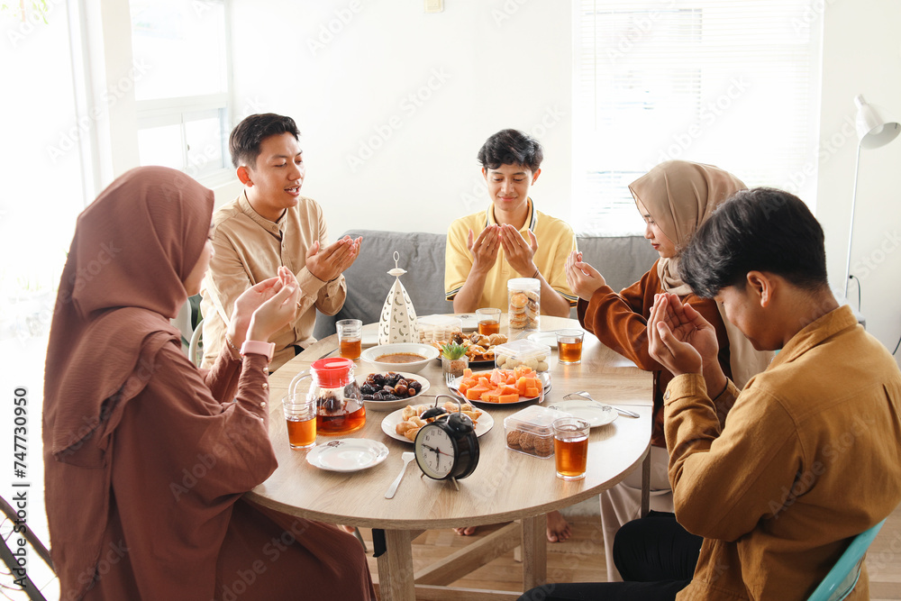Group of Asian muslim people sitting at dining table, raising hands and praying before eating together Group of Asian muslim people sitting at dining table, raising hands and praying before eating together