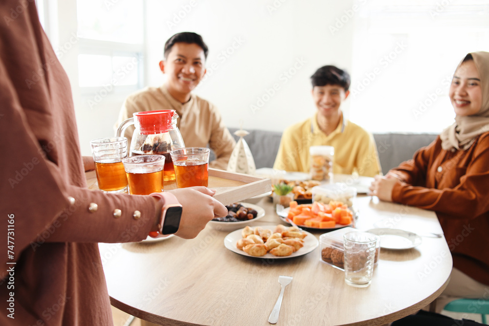 Muslim woman serving glasses of tea on wooden tray for friends during breakfasting in Ramadan