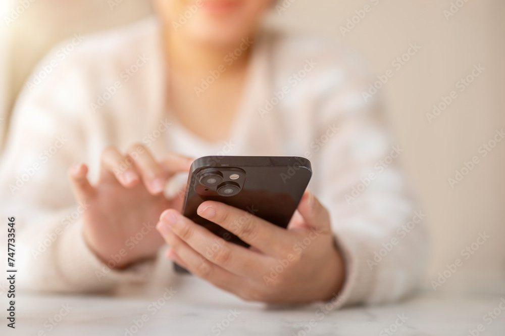 A woman using her smartphone while sitting at a table by the window in a coffee shop. A woman using her smartphone while sitting at a table by the window in a coffee shop.
