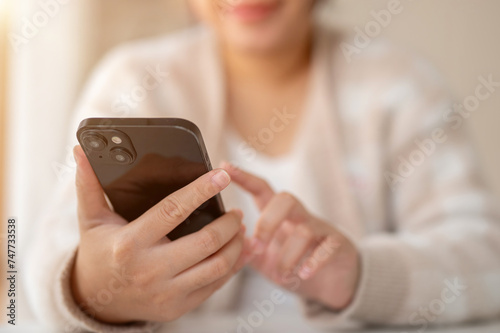 A woman using her smartphone while sitting at a table by the window in a coffee shop.