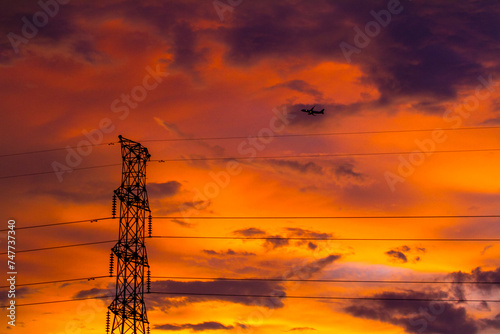 power lines at sunset with airplane in the background