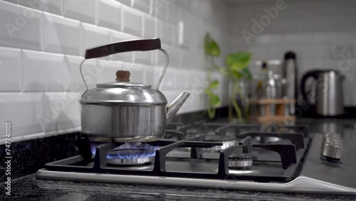 Pava hirviendo emanando vapor de agua sobre estufa a gas natural con fondo de hermosa cocina moderna photo