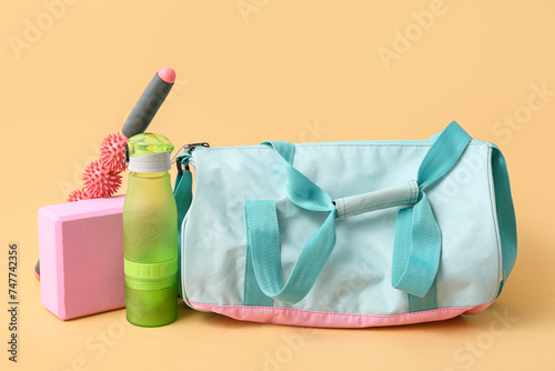 Sports bag with sportswear and workout equipment on beige background