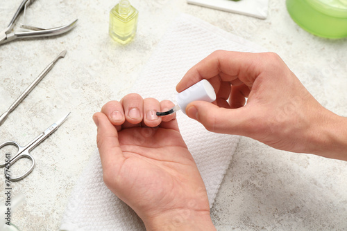 Male hands applying cuticle oil onto fingernails, manicure instruments and towel on light grunge background
