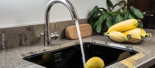 A granite kitchen sink with stainless steel two-handle faucet, filled with ripe bananas. The bananas are resting in the sink, ready to be washed or used for cooking and snacking.