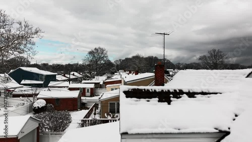 A low angle view of a suburban neighborhood after snowfall. It's a cloudy morning, and the neighborhood is quiet. The drone camera dolly in, and boom up as birds fly towards the camera. photo