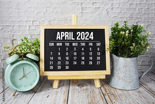 April 2024 monthly calendar and alarm clock on wooden background