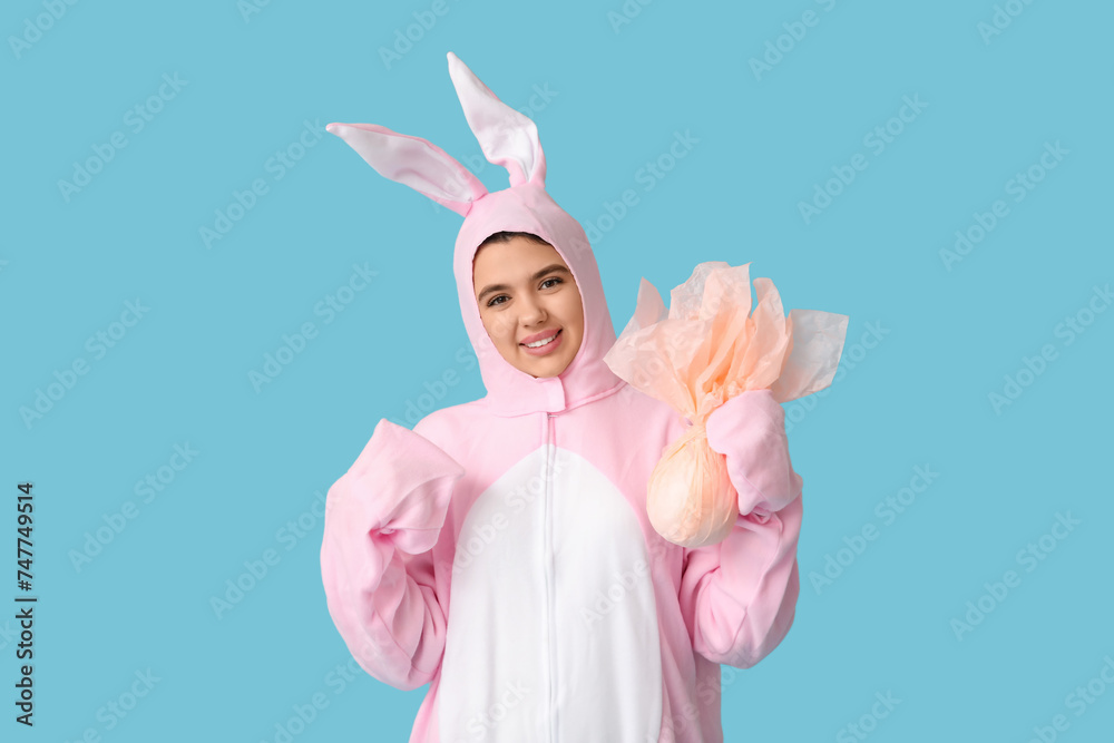 Beautiful young woman in bunny costume with Easter gift egg on blue background
