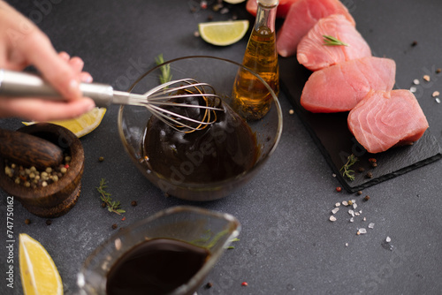 Woman mixing with whisk soy sauce and olive oil in a glass bowl making marinade to marinate Pieces of Fresh tuna Fish fillet