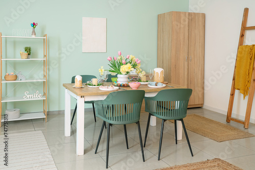 Light interior of festive dining room with Easter table setting  vase of flowers and chairs