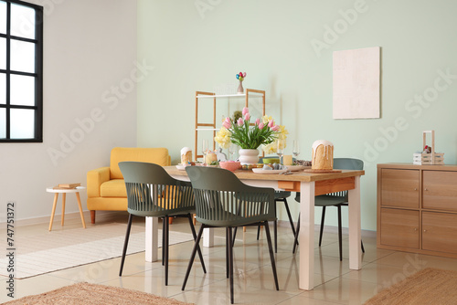 Light interior of festive dining room with Easter table setting  vase of flowers and chairs