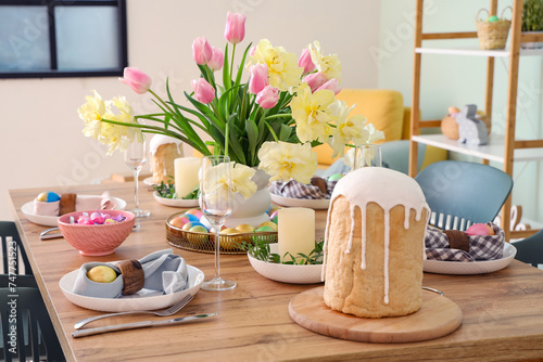 Stylish festive table setting, painted eggs, Easter cake and vase of flowers in dining room