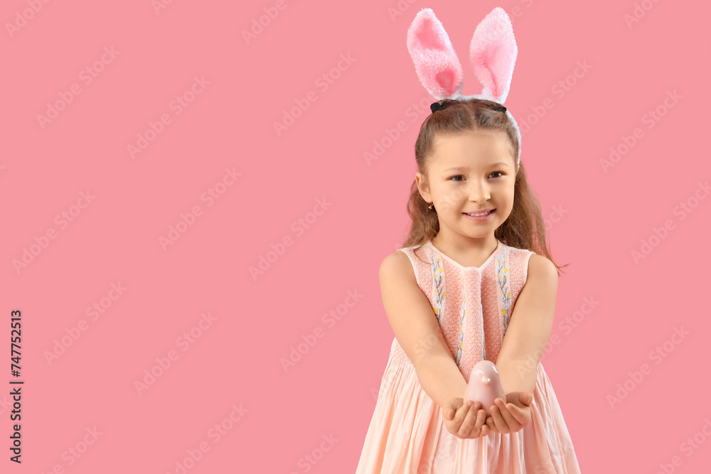 Cute little girl in bunny ears with bird on pink background. Easter celebration