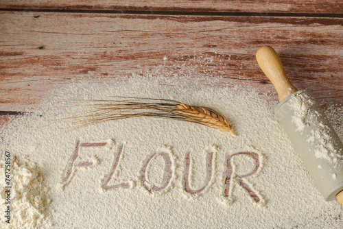 sifted flour on a wooden table with the word flour written on it, next to an ear of wheat and a rolling pin, wooden bottom and copy space