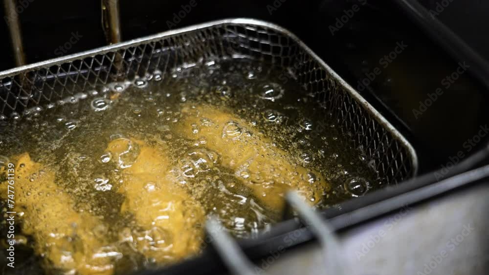 Three eggrolls in basket deep frying in hot oil, slider close up slow motion 4K
