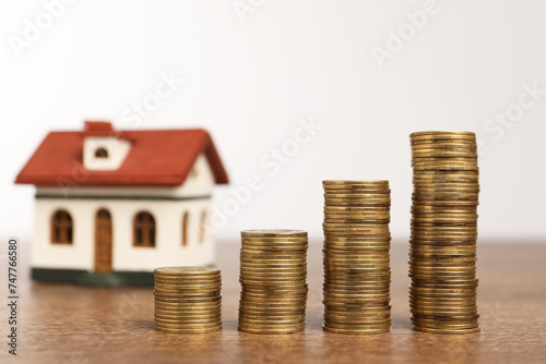 Mortgage concept. House model and stacks of coins on wooden table against white background, selective focus