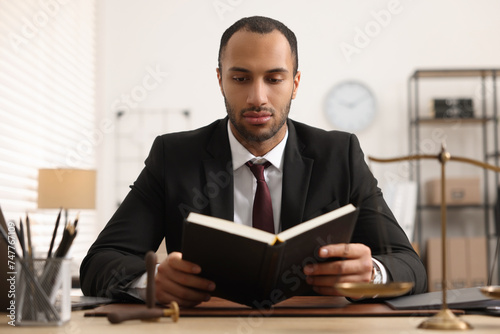 Serious lawyer reading book at table in office