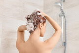 Young woman washing her hair with shampoo in shower, back view