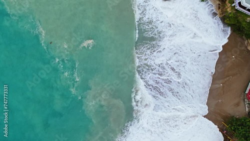 Dark brown sand in cove churns in undertow of strong wave swell in ocean, drone bird's eye view photo