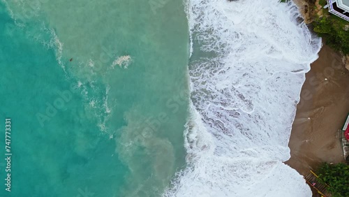 Dark brown sand in cove churns in undertow of strong wave swell in ocean, drone bird's eye view