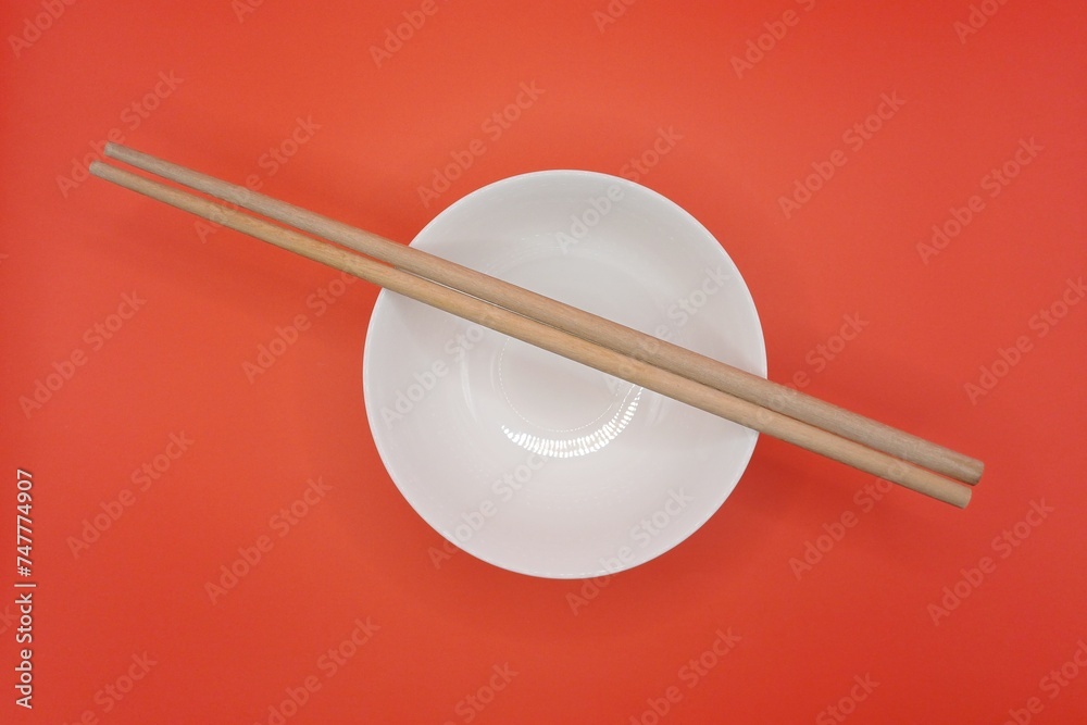 Close-up of white bowl and wooden chopsticks on red background. Close-up of white bowl and wooden chopsticks on red background.