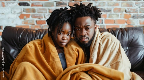 A man and a woman are sitting on a couch, wrapped in warm blankets.