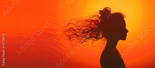 A woman stands with her hair blowing in the wind, creating a dynamic and energetic scene. The wind ruffles her hair, adding movement and life to the image.