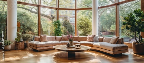 A front view of a living room filled with various furniture pieces  including a sofa  coffee table  armchairs  and shelves  illuminated by natural light streaming in through large windows.