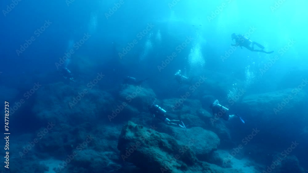 scuba divers exploring around a reef underwater deep blue water big rocks and bubbles ocean scenery scuba divers exploring around a reef underwater deep blue water big rocks and bubbles ocean scenery