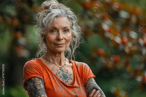 Beautiful old woman with tattoos and grey hair in orange t-shirt in the garden. Positive aging concept.