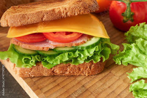 Sandwich with ham  cheese and vegetables on a wooden board. The concept is a student s breakfast. 