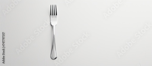 A small silver fork with two prongs rests on a white surface against a white background.
