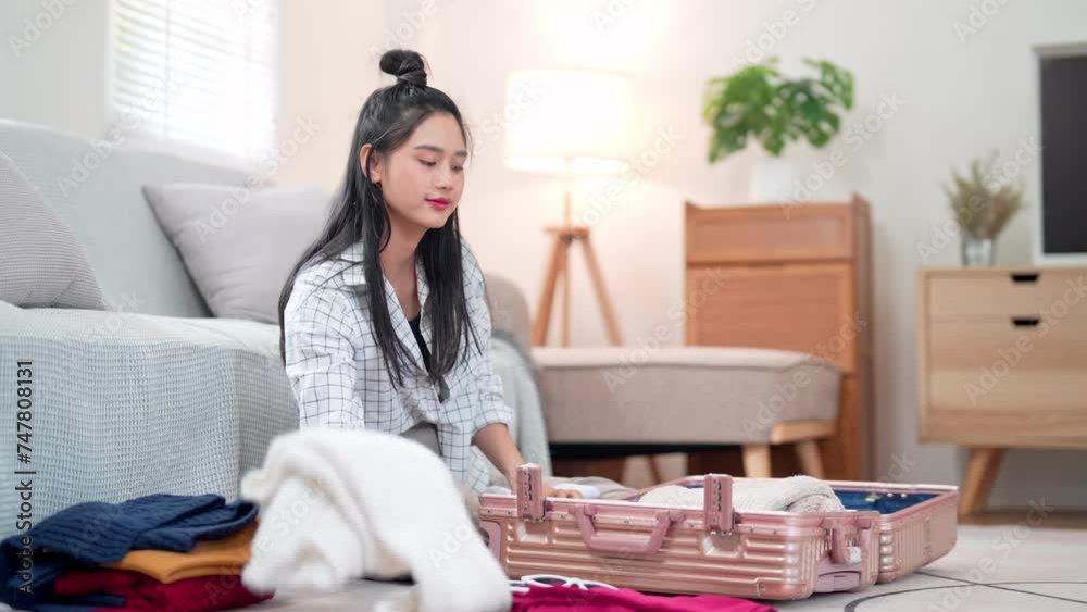 Asian woman organizing her belongings, packing them into a travel bag, getting ready for a holiday adventure Asian woman organizing her belongings, packing them into a travel bag, getting ready for a holiday adventure