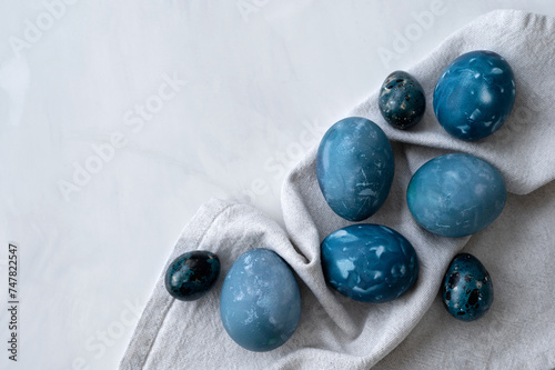 Creative naturally dyed blue Easter eggs on white marble tabletop and linen napkin, traditional holiday Easter food, aesthetic minimalist Scandinavian style