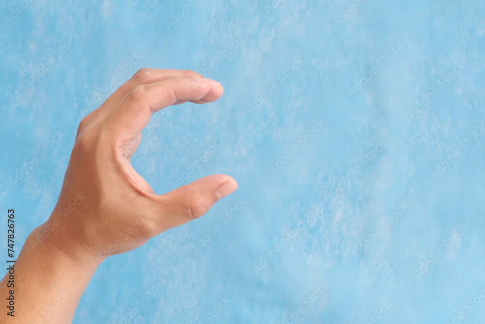 Young male Asian hand making letter C sign isolated on blue background.